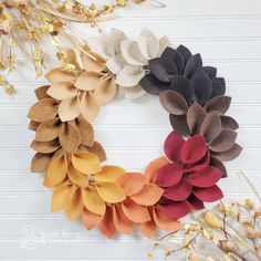 a wreath made out of felt flowers sitting on top of a white table next to dried plants