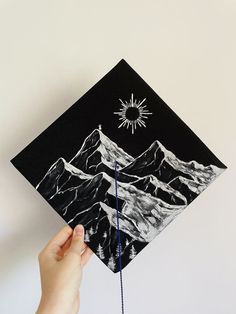 a hand holding up a black and white graduation cap with mountains in the back ground