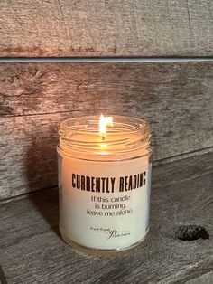 a candle that is sitting on a wooden table next to a piece of wood with the words currently reading