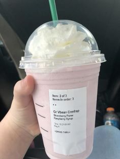 a hand holding up a pink drink with whipped cream on top