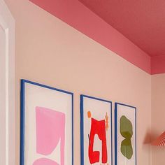 three paintings are hanging on the wall in a pink and blue room with a red lamp