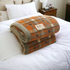 an orange and grey plaid blanket folded on top of a white bedspread in a hotel room