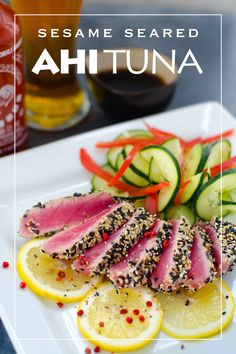 sesame seared ahutna with lemon slices and cucumbers on a white plate