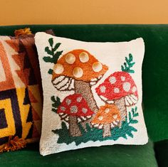 two pillows sitting on top of a green couch next to a pillow with mushrooms on it