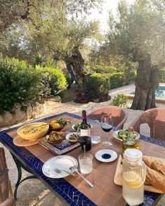 a table with food and wine on it in front of an outdoor swimming pool area