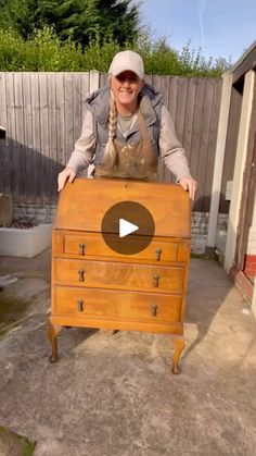 a woman standing behind a wooden dresser with an apron on it's head and smiling