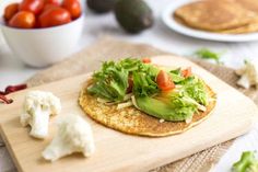 a tortilla topped with lettuce and tomatoes on a wooden cutting board