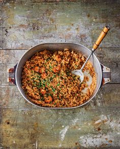 a large pot filled with food on top of a wooden table next to a fork