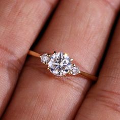 a woman's hand holding an engagement ring with three diamonds on top of it