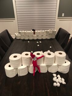 the elf is surrounded by toilet paper on the dining room table with several rolls of toilet paper in front of him