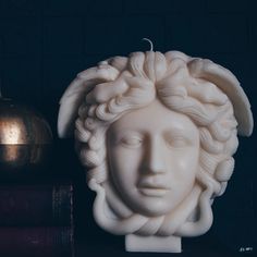 a white busturine sitting on top of a table next to some books and a candle