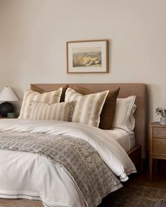 a bed with white sheets and pillows in a bedroom next to a painting on the wall