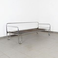 a metal bench sitting on top of a tile floor next to a white wall in an empty room