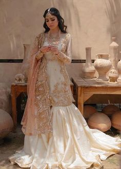 a woman in a white and gold dress standing next to vases on a table