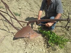 a man kneeling down in the dirt with an old shovel and some plants growing out of it