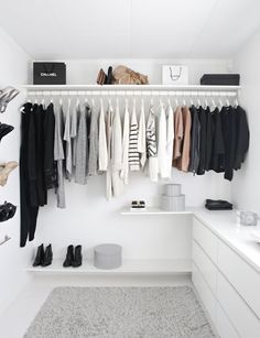 a white closet with clothes and shoes hanging on the wall next to a counter top