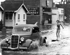 a woman is standing on a surfboard in the water next to an old car