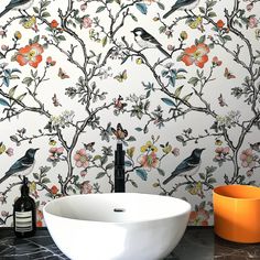 a white bowl sitting on top of a counter next to a wall with flowers and birds