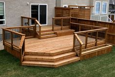 a wooden deck with stairs and railings in front of a house on the grass