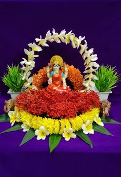 the statue is surrounded by flowers and plants on a purple tablecloth with blue background