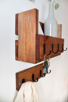 two wooden hooks are hanging on the wall with key holders attached to them and a white vase in the background