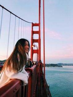 a woman standing on the side of a bridge next to the ocean and looking into the distance