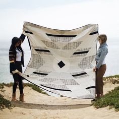 two women standing on the beach holding up a large white and black piece of cloth