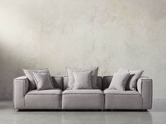 a gray couch with pillows on it in front of a white wall and concrete floor