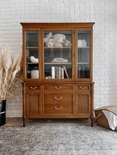 a wooden china cabinet with glass doors and drawers in front of a white brick wall