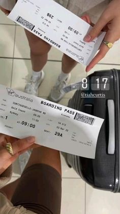 two people standing next to each other in front of a luggage bag and holding tickets