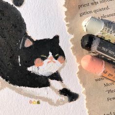 a black and white cat laying on top of a piece of paper next to some crayons