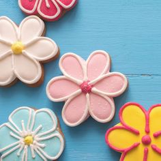 four decorated cookies on a blue surface with pink, yellow and white flowers in the middle