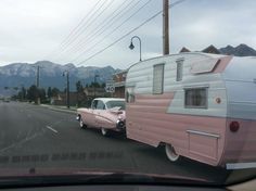 an old pink and white trailer parked on the side of the road next to a car