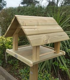 a wooden bird house sitting on top of a bench in front of some bushes and trees