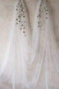 two white veils hanging on a wall with flowers and leaves attached to the side