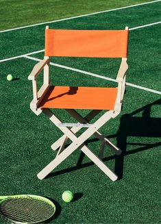 an orange chair sitting on top of a tennis court next to a racquet