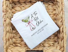 a personalized cocktail napkin on top of a wicker basket with an olive in it