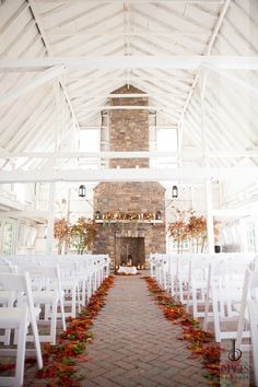 an indoor wedding venue with white chairs and candles on the aisle leading up to the alter