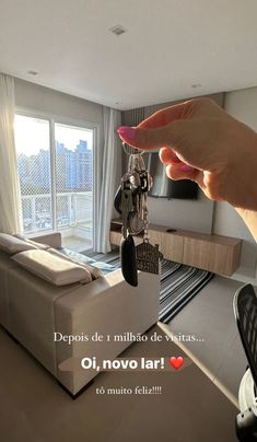 a person holding keys in front of a living room with a large window and city view