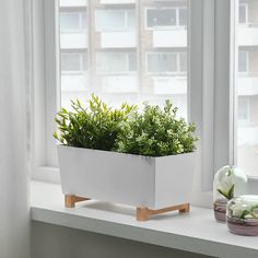 a white planter sitting on top of a window sill next to a potted plant