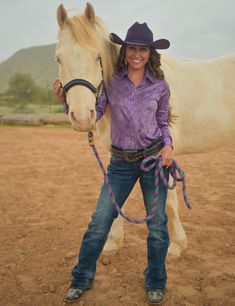 a woman standing next to a horse wearing a purple shirt and cowboy hat with a rope