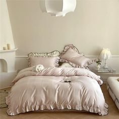 a bed with pink comforter and pillows in a white room next to a fireplace