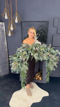 a woman standing in front of a fireplace holding a wreath with white flowers and greenery