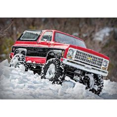 a red truck driving through the snow on top of a pile of snow covered ground