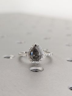 an engagement ring with a pear shaped diamond surrounded by small white and black dots on a gray surface