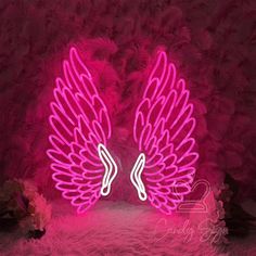 two neon angel wings on a pink fur background with the word love written in white