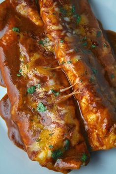 two enchiladas on a plate with sauce and parsley