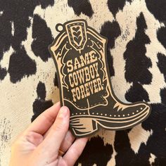 someone holding up a sticker that says same cowboy forever on the back of a cow print fabric