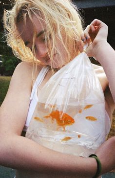 a woman holding a plastic bag filled with goldfish