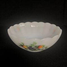 a white bowl with fruit painted on the side and green leaves in the middle, sitting on a black surface